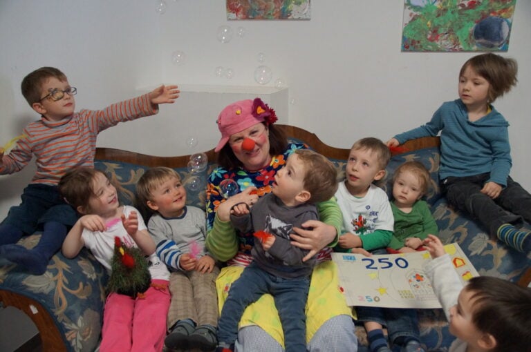Viele Kleinkinder sitzen mit einem weiblichen Clown auf einem Sofa