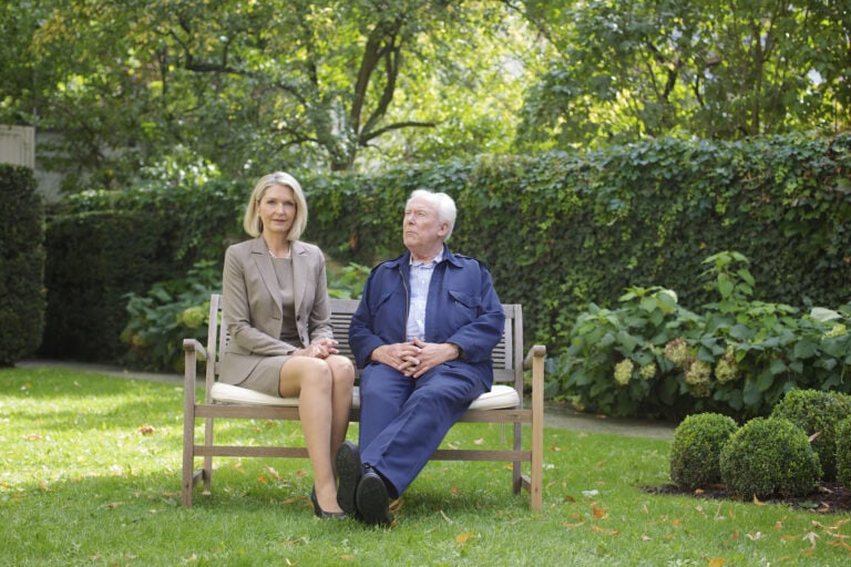 Frau und älterer Mann sitzen auf einer Bank in einem grünen Garten