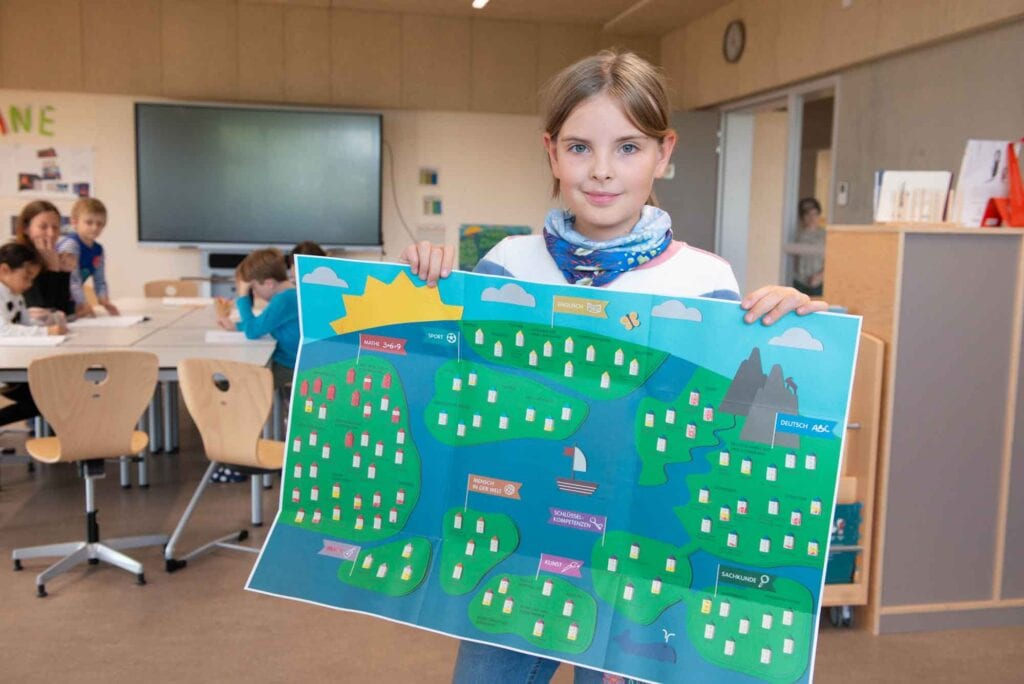 Eine Schülerin steht im Klassenzimmer und präsentiert die element-i Lernweltkarte.