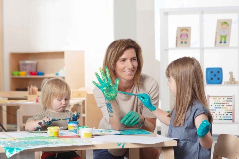 Ein Junge, ein Mädchen und eine Frau sitzen an einem Tisch und malen die Hände der Frau an.